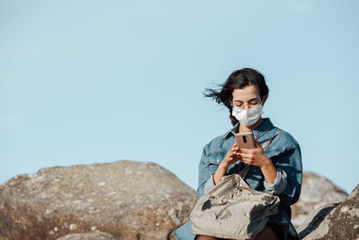 Young man holding rock against clear blue sky