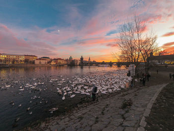 Scenic view of lake by buildings against sky during sunset