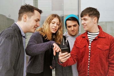 Young man using smart phone while standing on laptop