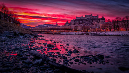 Scenic view of sea by buildings against sky at sunset