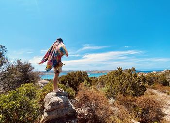 Rear view of man standing on rock against blue sky