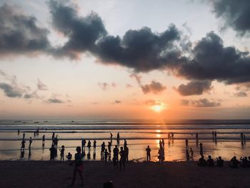 Silhouette people on beach against sky during sunset