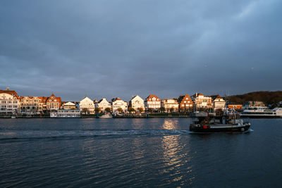 Buildings at waterfront against cloudy sky