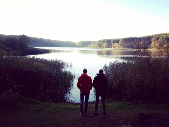 Rear view of men standing on shore against clear sky