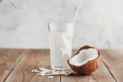 A glass of fresh organic coconut water, milk on a wooden table and a ripe half of a coconut nearby.