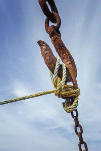 Low angle view of rope tied up of rusty chain against sky