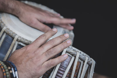 Cropped hands of man playing tabla against black background