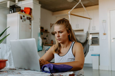 Focused young female in casual wear browsing modern netbook while sitting at table in contemporary apartment