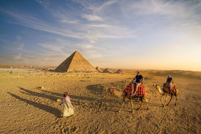 People riding camel in desert against pyramids 