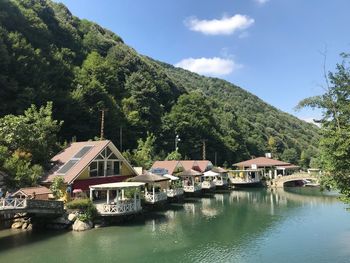 Houses by river and trees against sky