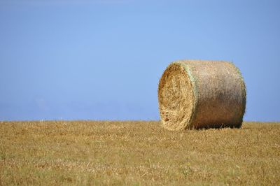 Hay bales on field against clear blue sky