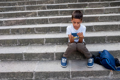Full length of boy using phone while sitting on steps