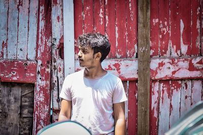 Young man looking away while standing against wall