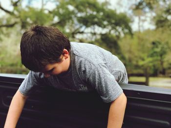 Boy leaning on railing against trees