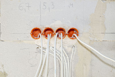 Orange, round junction box mounted in the white wall with protruding electric cables.