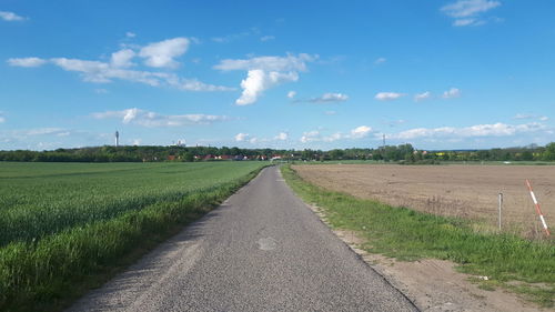 Empty road amidst field against sky