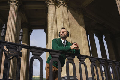 Businessman with headphones holding coffee cup leaning on railing at kazan cathedral at saint petersburg, russia