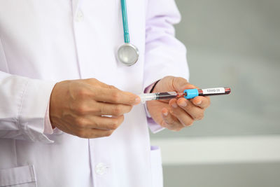 Midsection of doctor holding syringe with blood sample