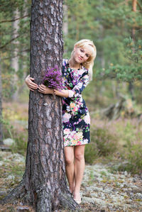 Young woman holding flowers with tree trunk in forest