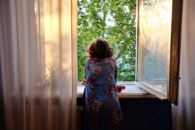 Rear view of woman standing by window at home