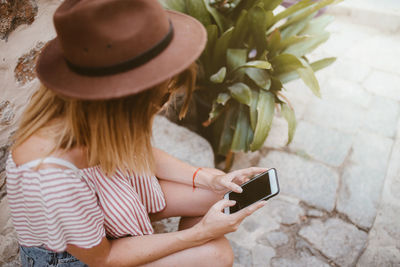 Unrecognizable woman sitting with hat watching her mobile phone