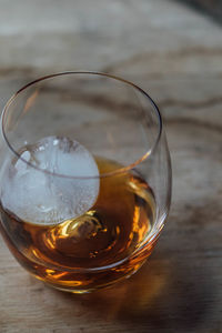 Close-up of whiskey in glass with ice sphere on bourbon barrel 