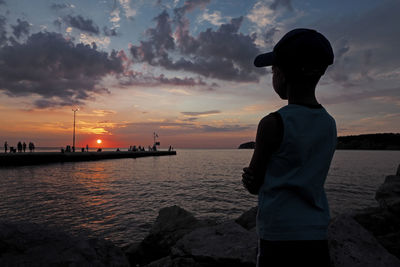 Boy looking at sea against sky during sunset
