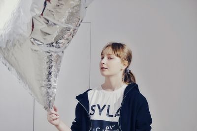 Teenage girl holding helium balloon against wall