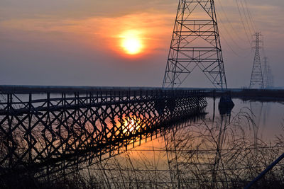 Silhouette bridge over sea against sky during sunset