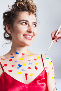 Cropped hand of woman applying paint on female friend against white background