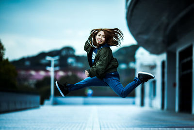 Full length of a young woman jumping against building