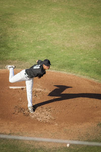 Teen baseball player in black and white uniform in full wind up on the mound