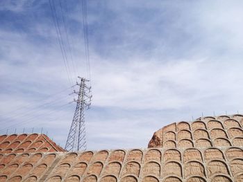 Low angle view of built structure and electricity pylon against sky