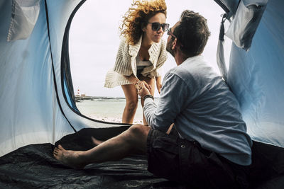 Young man kissing woman while sitting in tent at beach