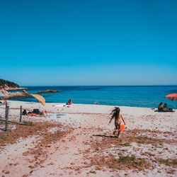 People on beach against clear blue sky