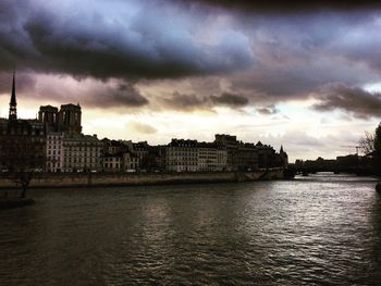 Buildings by river against sky at dusk