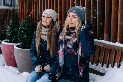 Portrait of two women friends on a winter snowy day sitting on a bench and enjoying the weather.