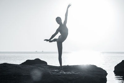 Woman dancing on rock against sea during sunny day