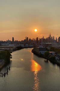 Scenic view of river by buildings against sky during sunset