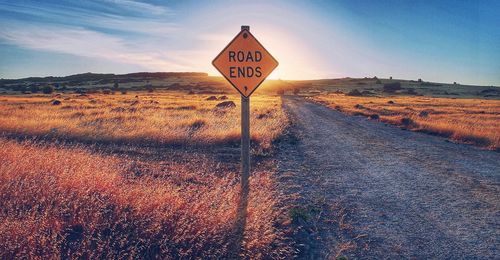 Road sign on landscape against sky during sunset