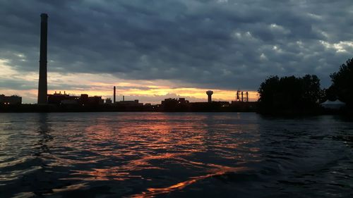 River by illuminated city against dramatic sky