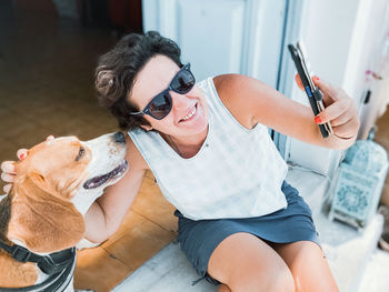 Portrait of young woman using mobile phone, sitting down with dog and smiling 