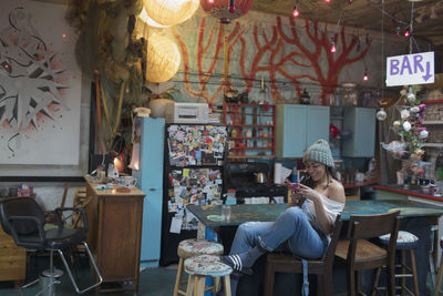 Young woman sitting in kitchen typing on her smartphone