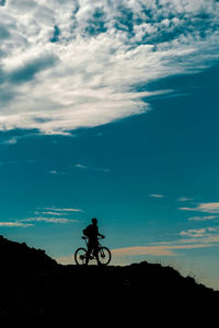 Silhouette person riding bicycle against sky