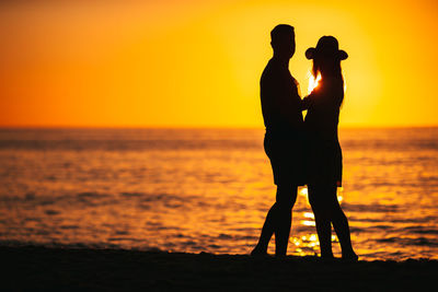 Silhouette woman walking at beach against sky during sunset