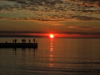 Silhouette people on sea against sky during sunset