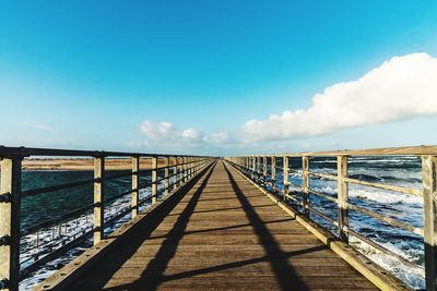 Footbridge over sea against blue sky