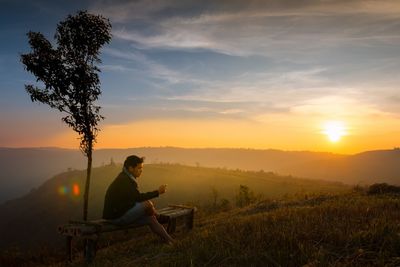 Man sitting on bench against sky during sunset