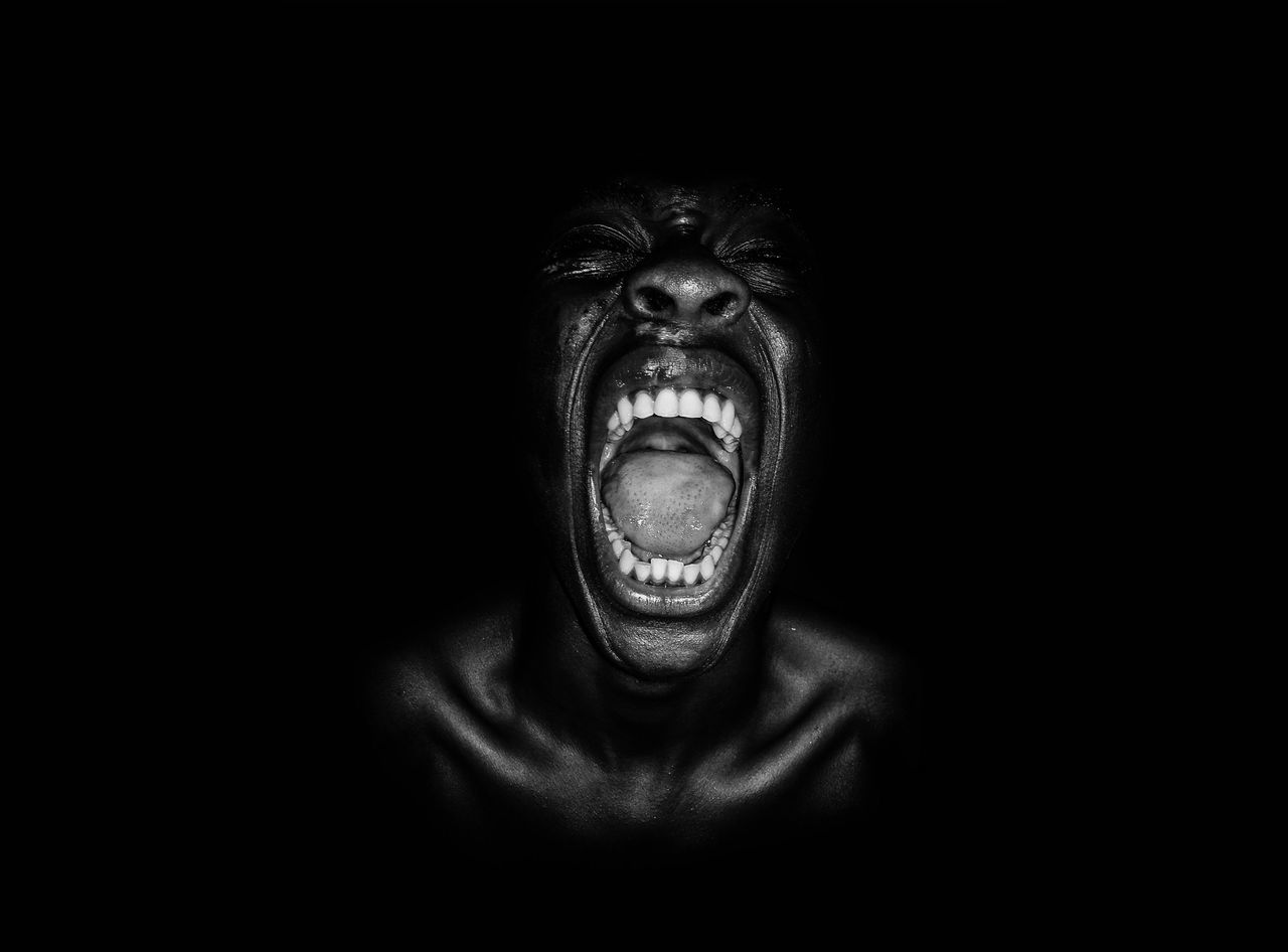 black background, negative emotion, portrait, anger, mouth open, mouth, primate, aggression, shouting, studio shot, frustration, emotion, furious, people, indoors, looking at camera, front view, facial expression, ape, dark, human teeth, human face