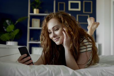 Young woman using mobile phone on bed at home